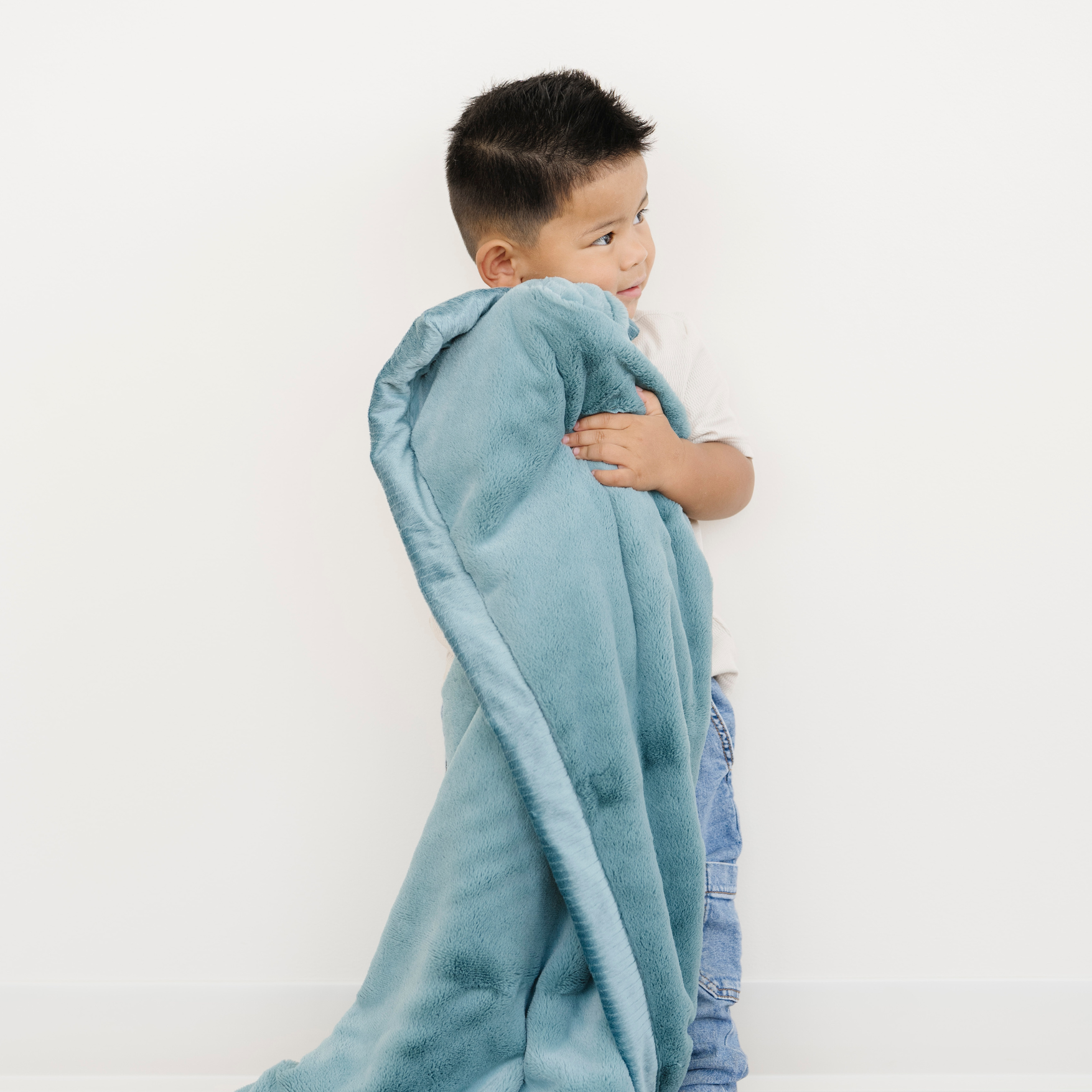 Toddler boy snuggled with Saranoni Lush Toddler Blanket in Mineral Blue. 