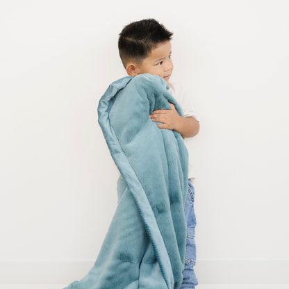 Toddler boy snuggled with Saranoni Lush Toddler Blanket in Mineral Blue. 