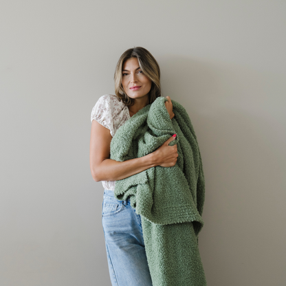 Woman holding olive green cozy bamboni blanket snuggled. 