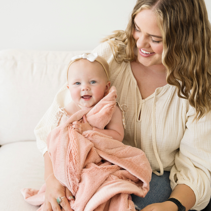Mom sitting with baby girl snuggled with Blossom lush receiving baby blanket. 