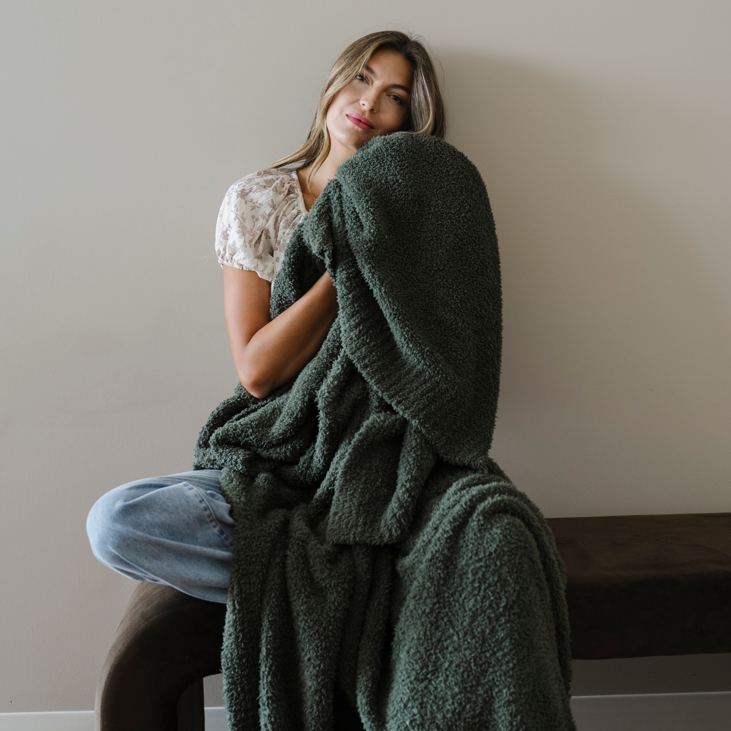 Woman sits wrapped in a juniper green extra large bamboni blanket.