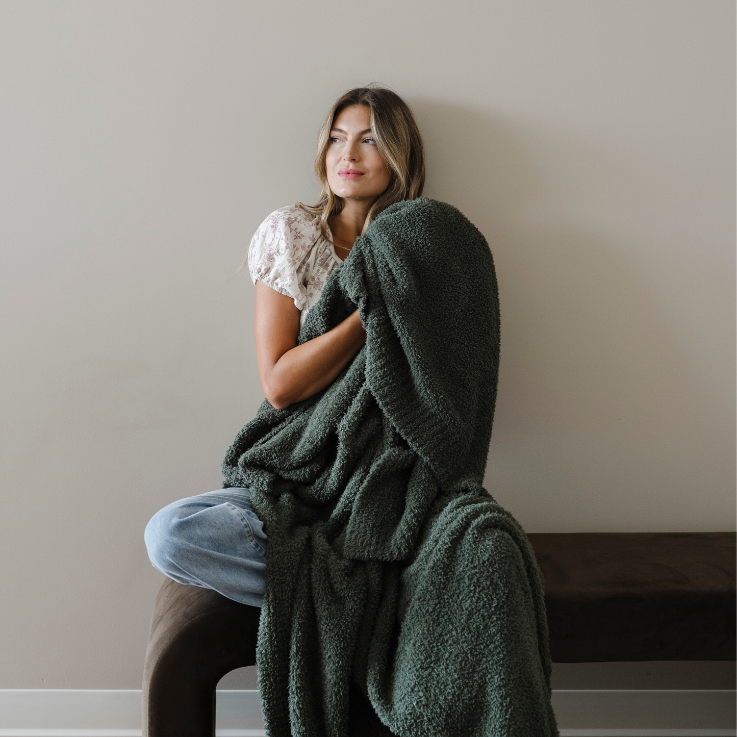 Woman sitting, snuggled with a juniper green bamboni extra large cozy blanket.