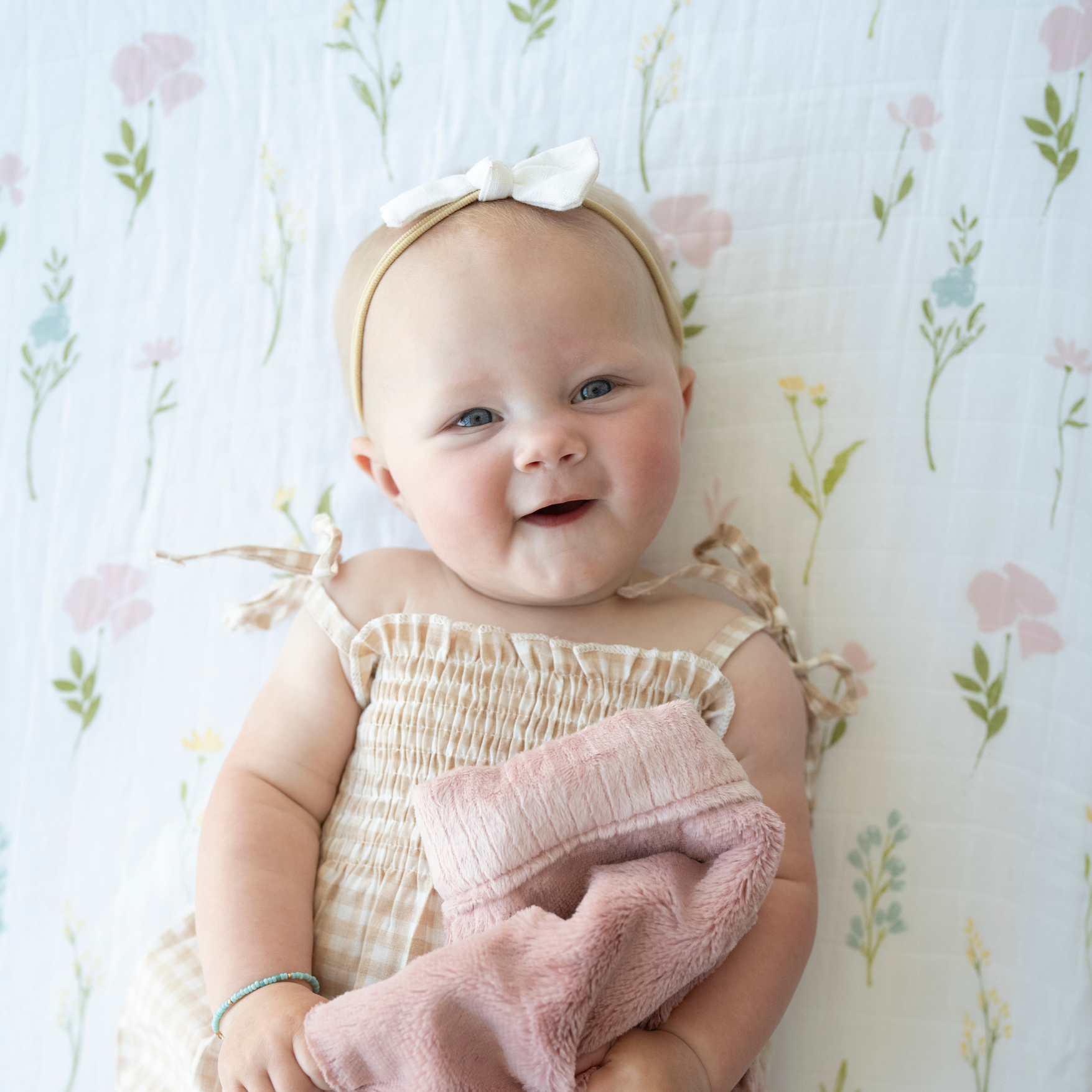Baby girl snuggled with Saranoni baby blanket while laying on Floral Fields Cotton Muslin crib sheet. 