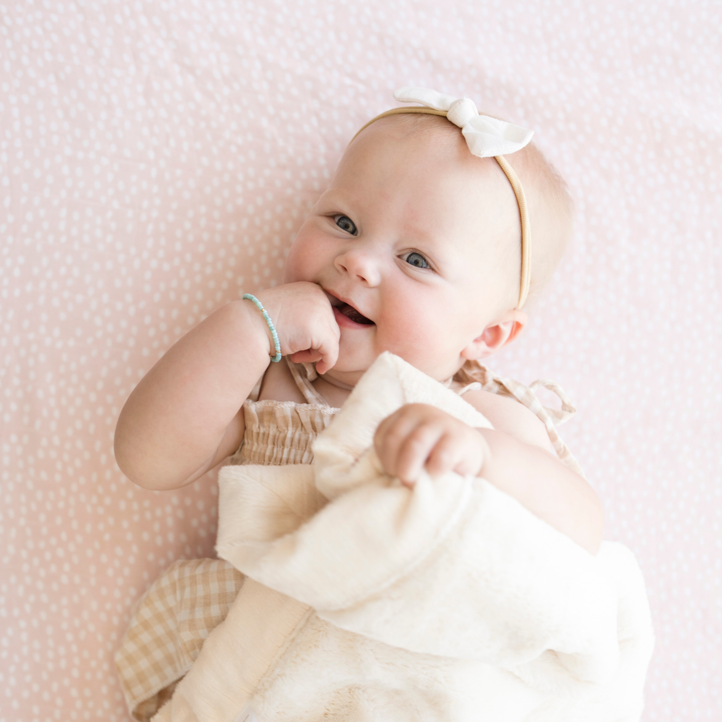 Baby girl snuggling with Saranoni Baby blanket while laying on Fallen Petal Cotton Muslin Crib Sheet. 