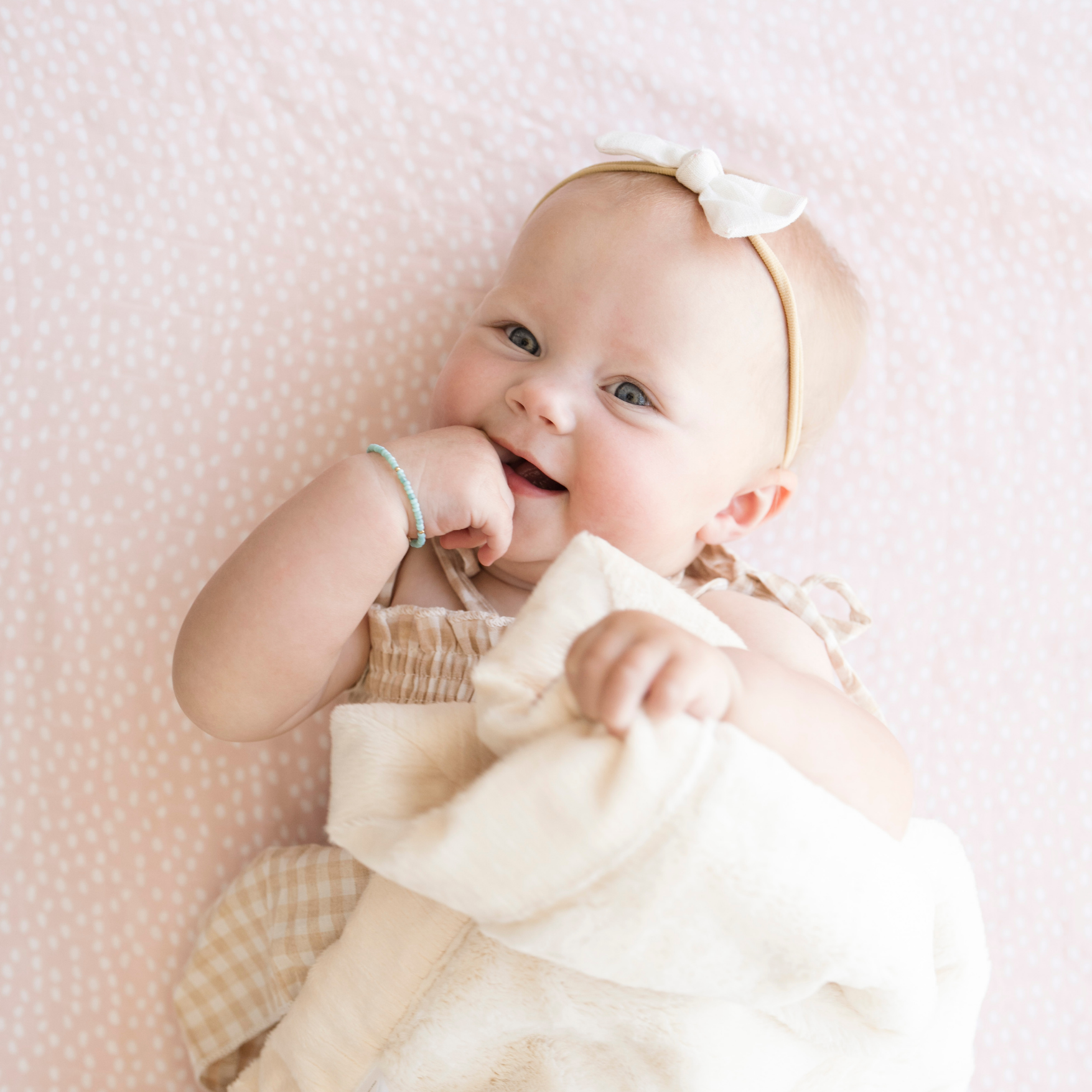 Baby girl snuggling with Saranoni Baby blanket while laying on Fallen Petal Cotton Muslin Crib Sheet. 