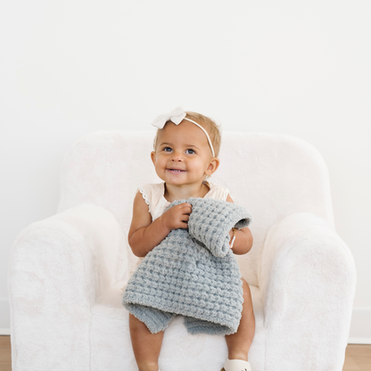 Toddler girl snuggled with elm green waffle knit mini blanket. 