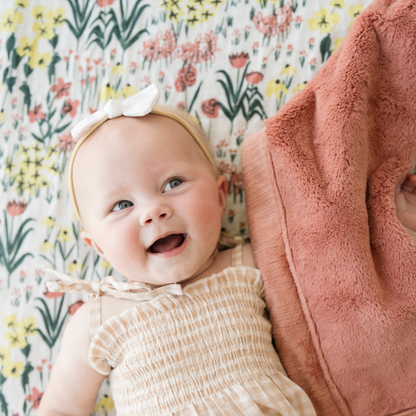 Baby girl laying on Roadside Picks Cotton Muslin crib sheet with baby blanket.