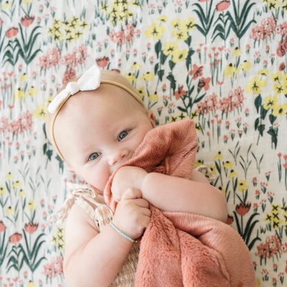 Baby girl snuggled with baby blanket laying on Cotton Muslin Roadside Picks crib sheet.