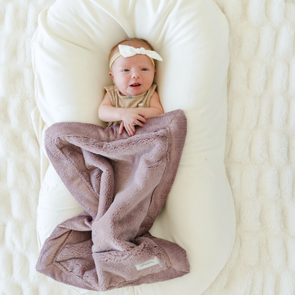 Baby girl snuggled with Bloom Lush Mini blanket. 