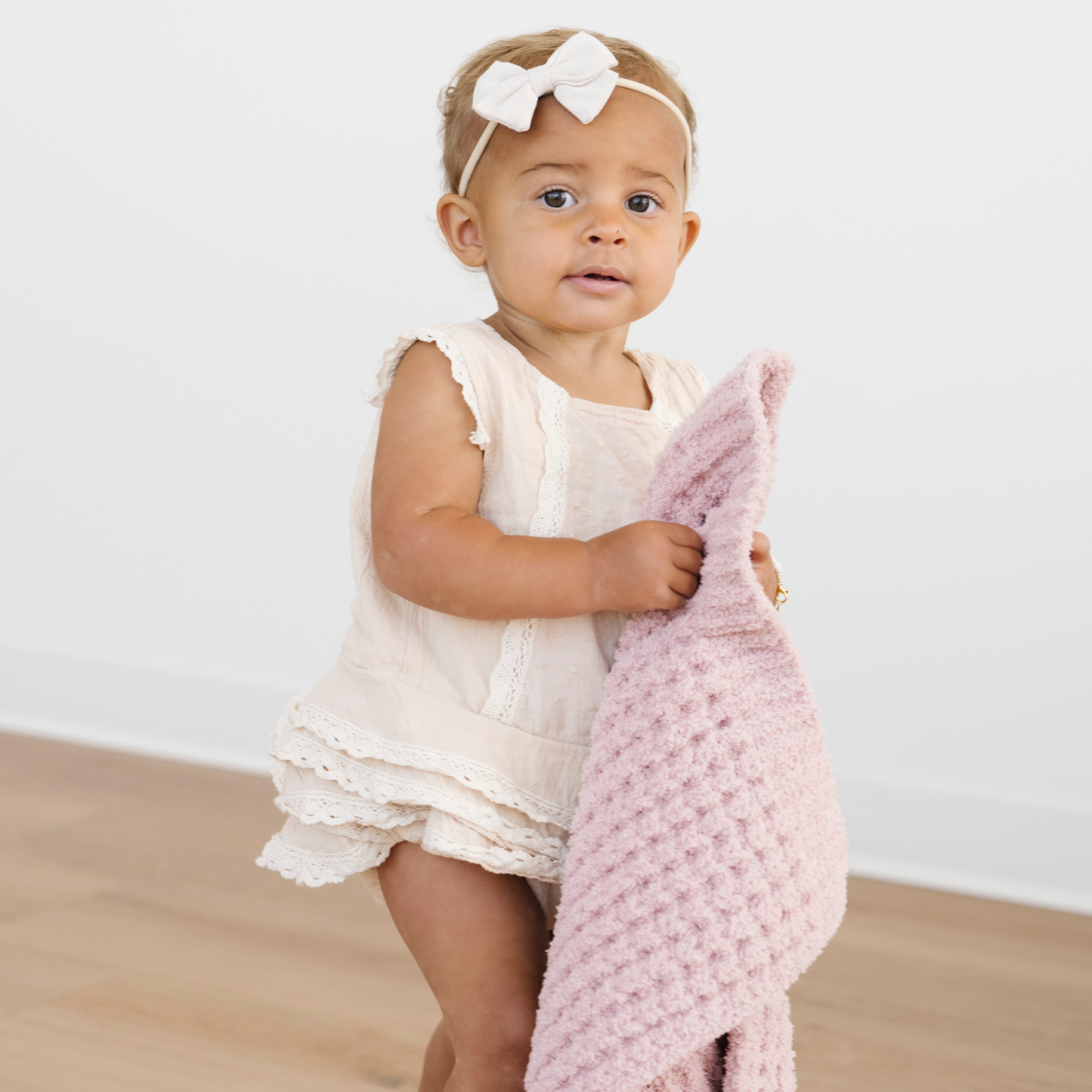 Toddler girl walks holding a pink waffle knit mini blanket. 
