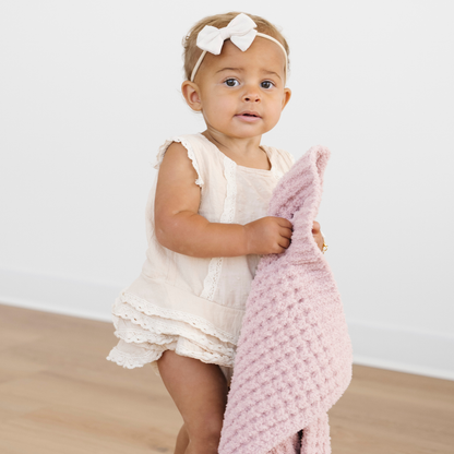 Toddler girl walks holding a pink waffle knit mini blanket. 
