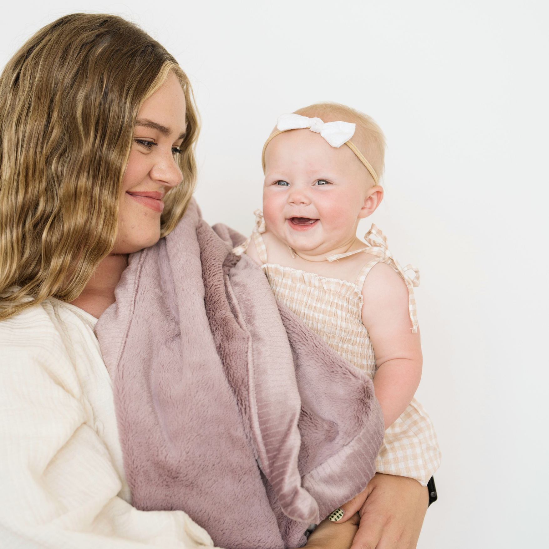 Mom holding baby girl, snuggled in Bloom lush receiving bay blanket. 