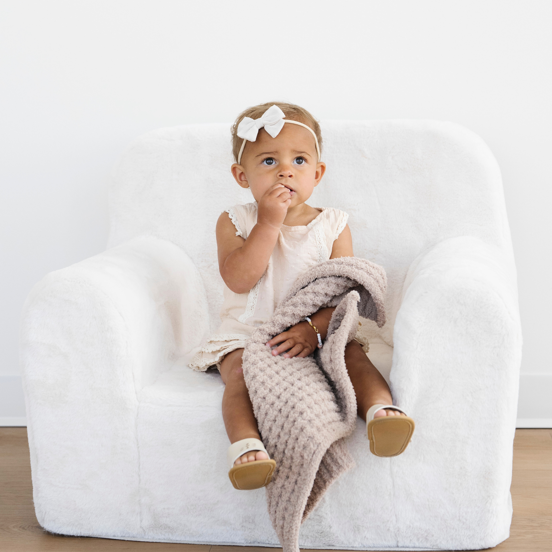 Toddler girl sitting in a chair with a wheat waffle knit mini blanket. 