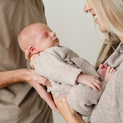 Newborn baby wearing taupe bamboni lite outfits being held by mom and dad. 