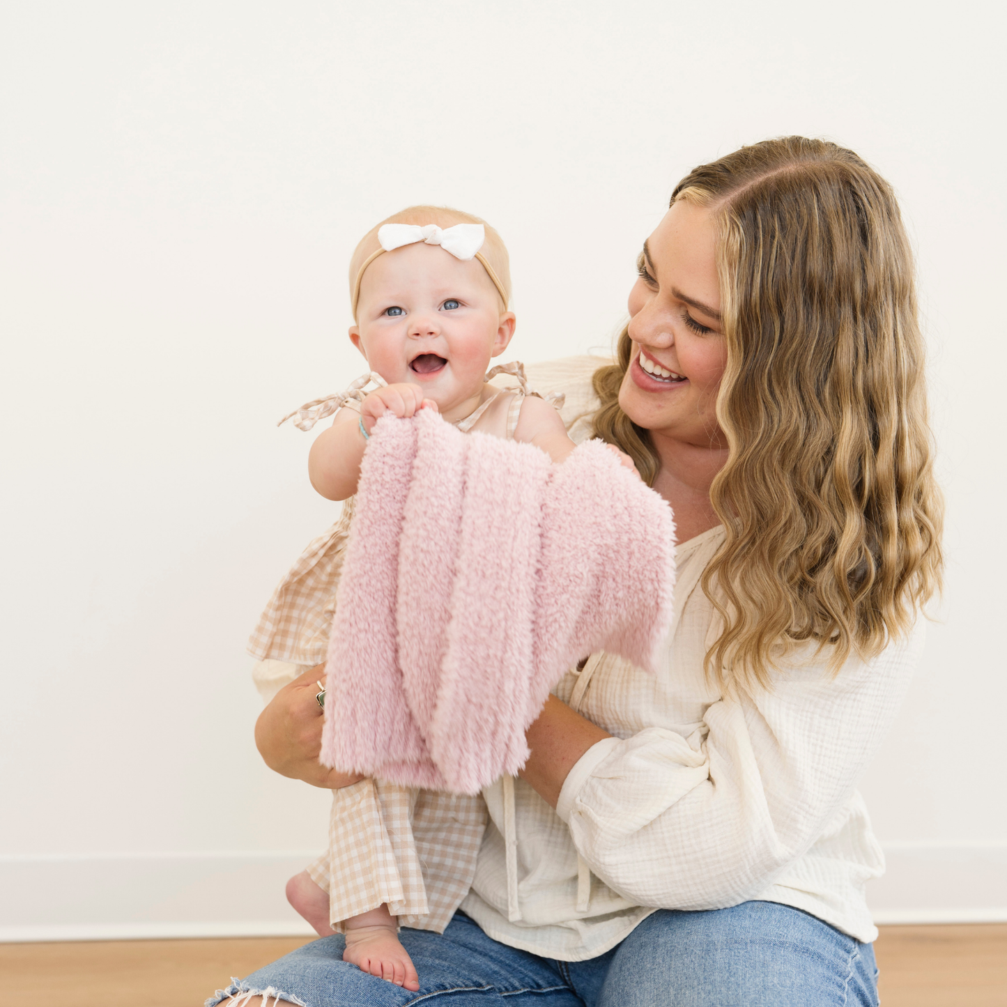 Mom holding baby girl snuggled with Light Pink Bamboni® Receiving soft baby blanket. 