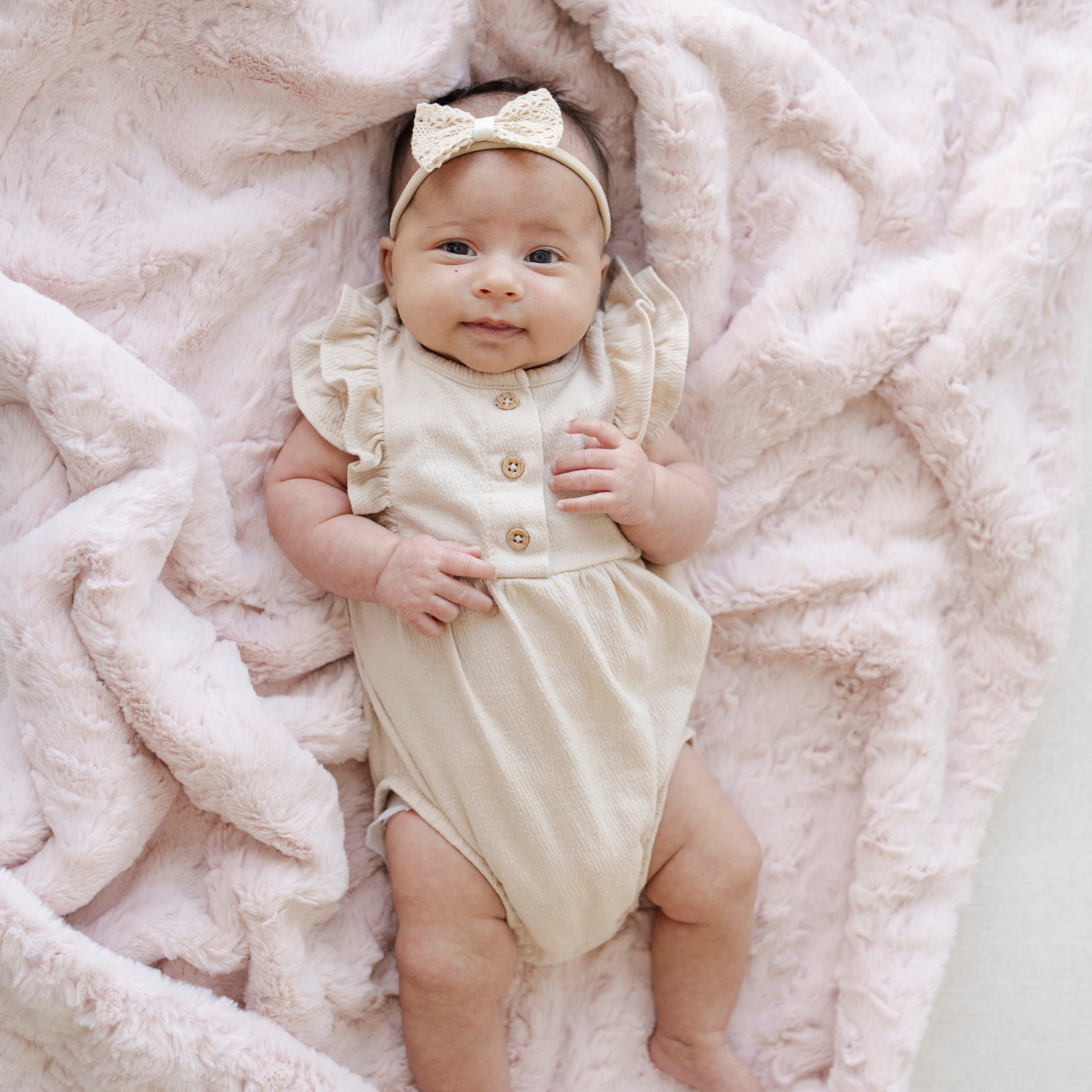 Baby girl laying on top of a blush pink dream faux fur receiving baby blanket. 