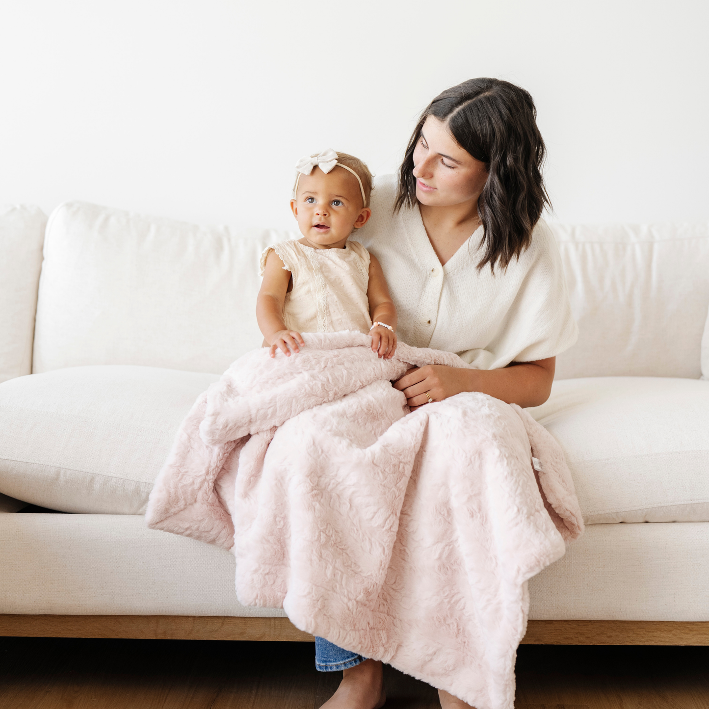 Mom holding little girl snuggled with a blush pink dream faux fur receiving baby blanket. 