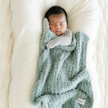 Baby boy snuggled with Ribbed Bamboni® mini blanket in Surf color. 