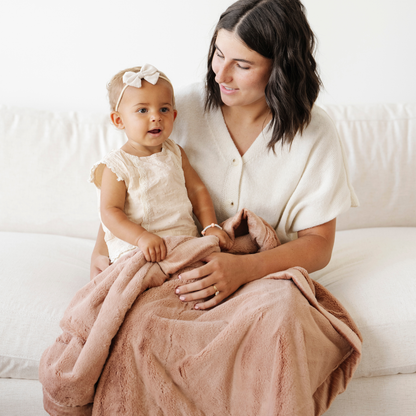 Mom holds little girl snuggled with a rosy pink lush receiving soft baby blanket. 
