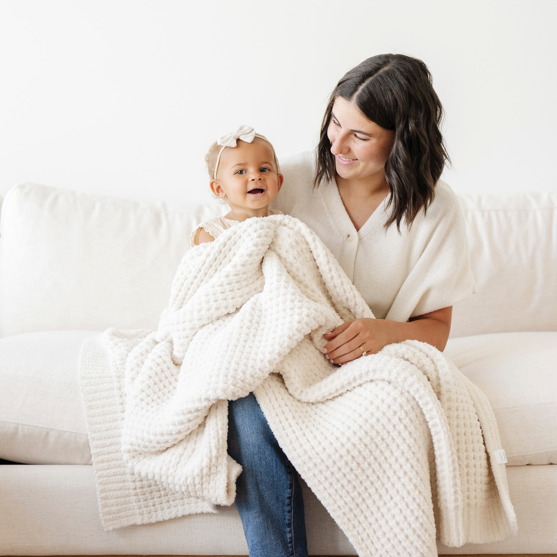 Mom holds little girl snuggled with a cream waffle knit receiving baby blanket. 