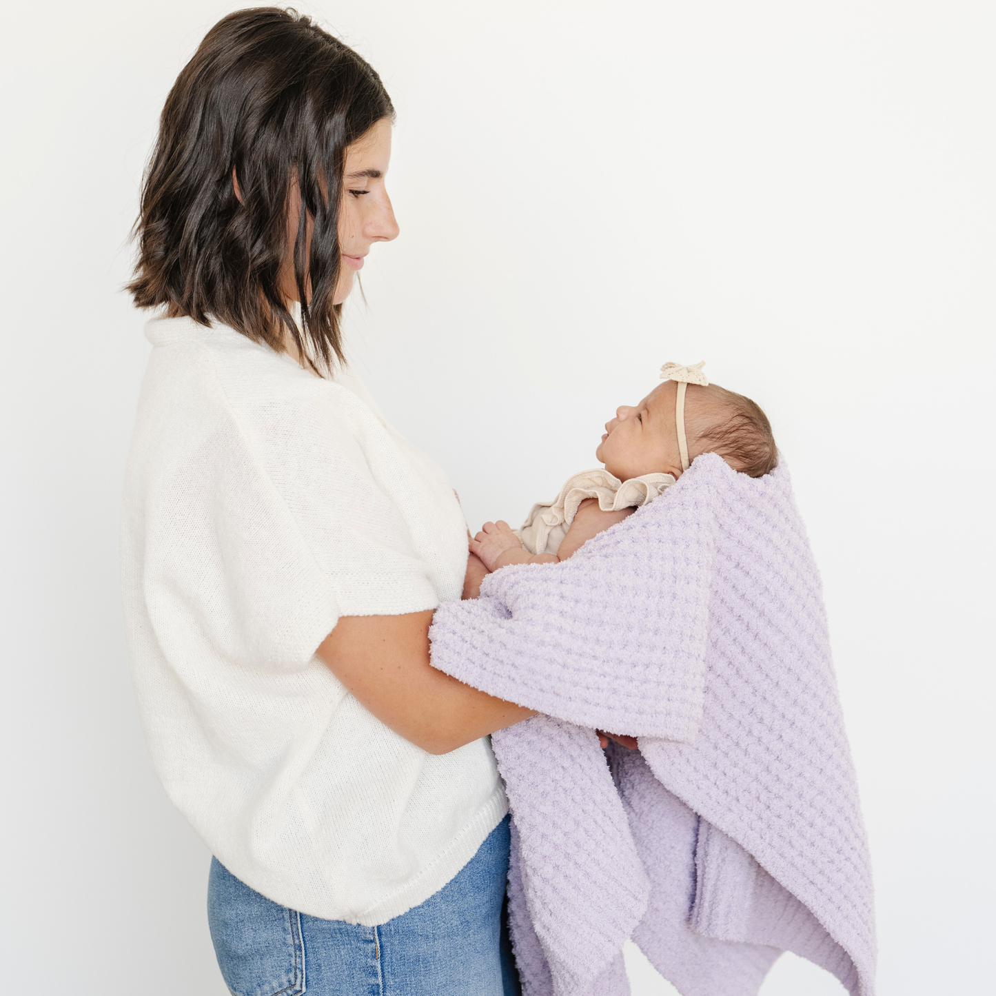 Mom holds baby girl wrapped in a purple waffle knit receiving baby blanket. 
