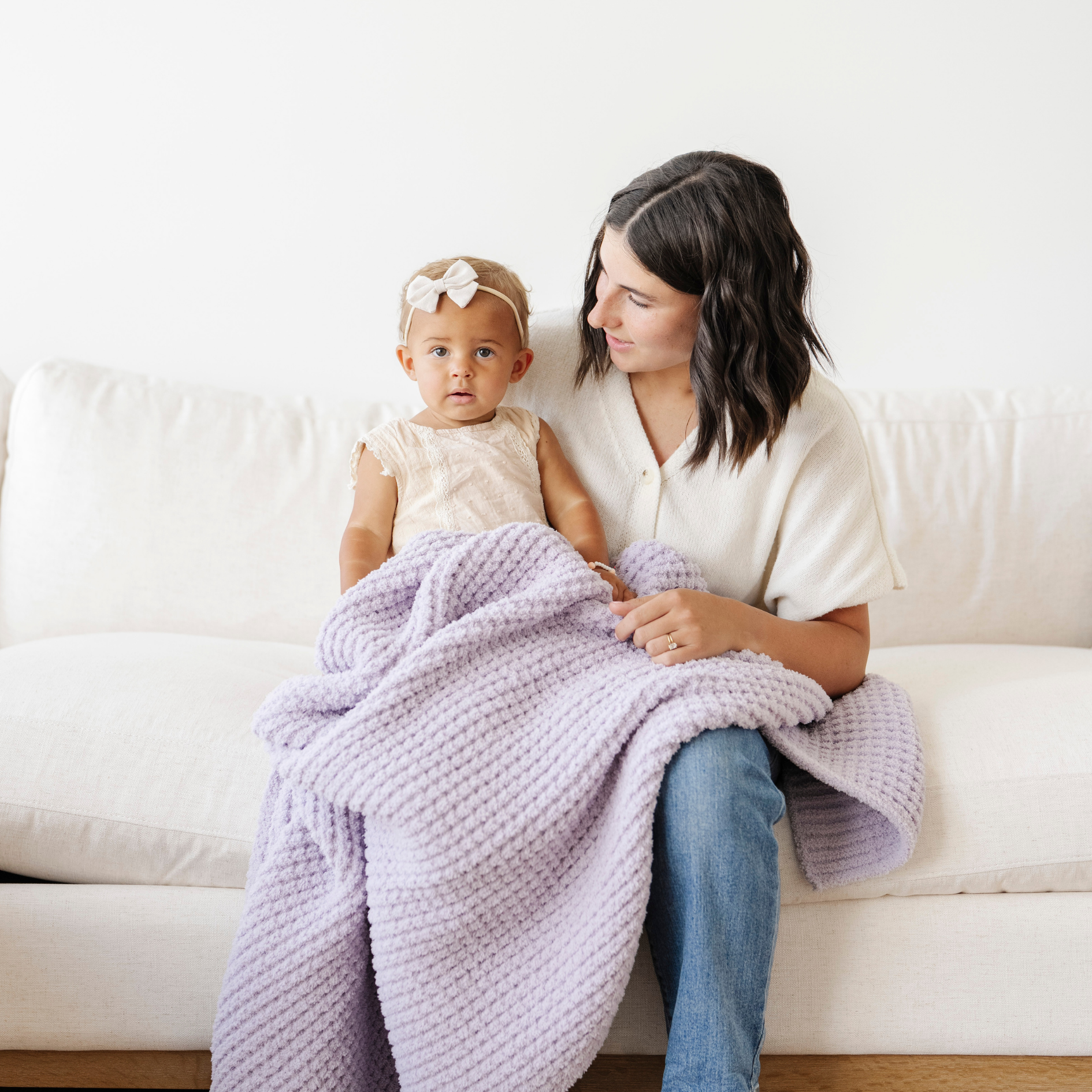 Mom holds little girl snuggled with a soft receiving baby blanket that is purple. 