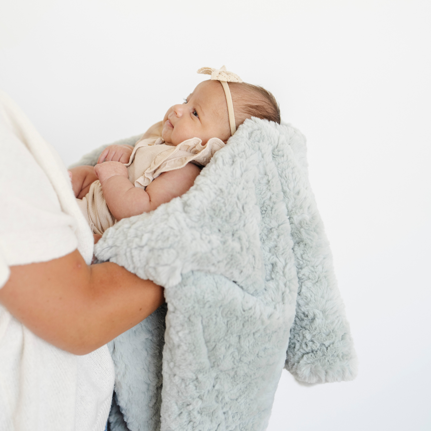 Mom holding baby girl snuggled in a mint green dream faux fur receiving blanket. 