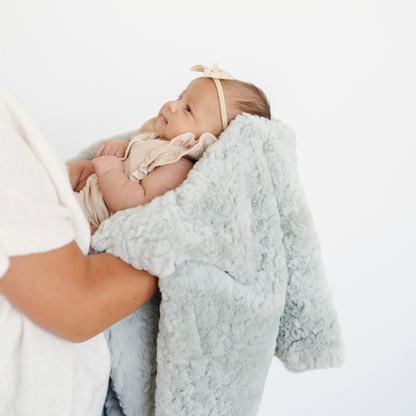 Mom holding baby girl snuggled in a mint green dream faux fur receiving blanket. 
