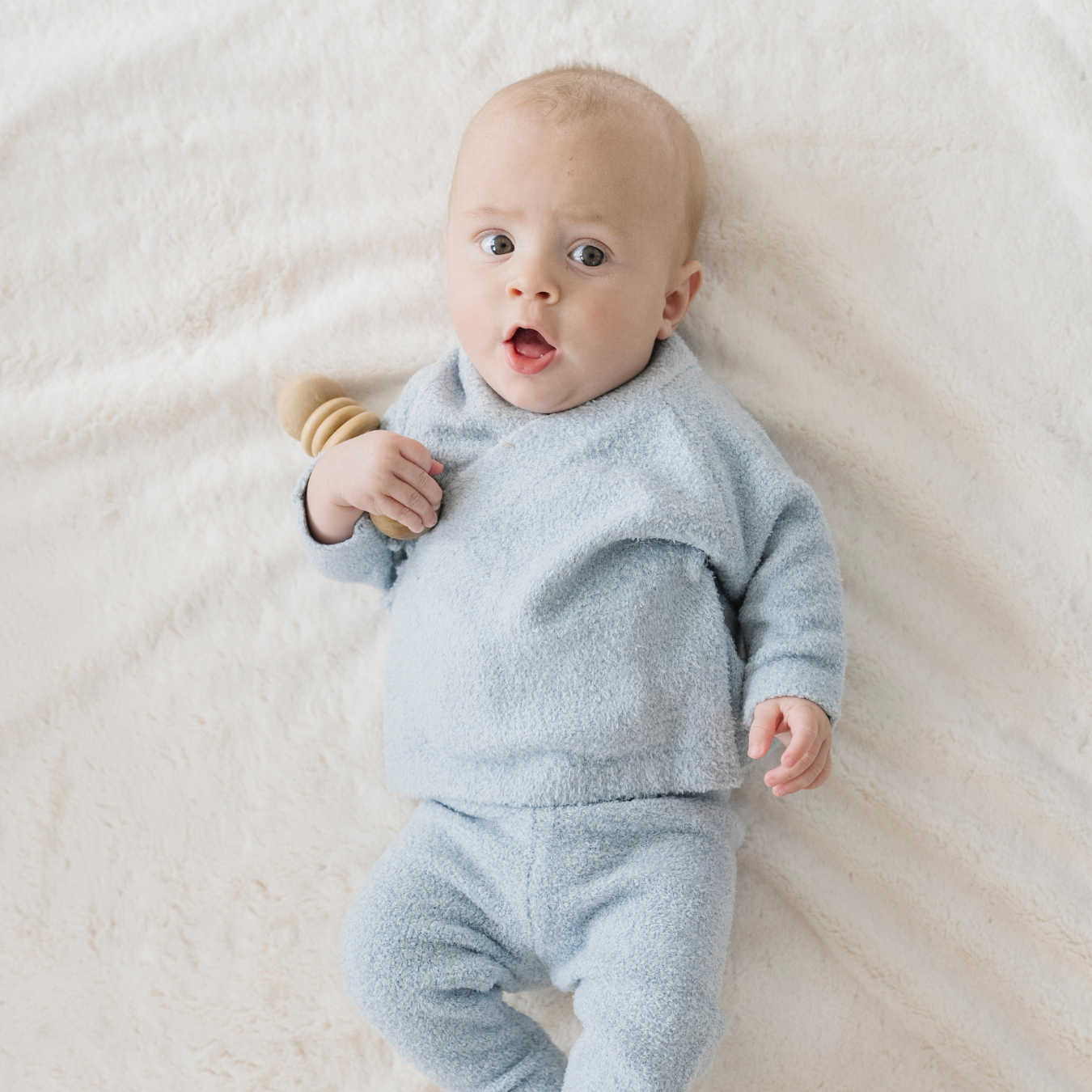 Baby in a light blue outfit lying on a white blanket
