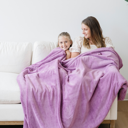 Mom and daughter snuggled on couch with a purple lush xl blanket. 