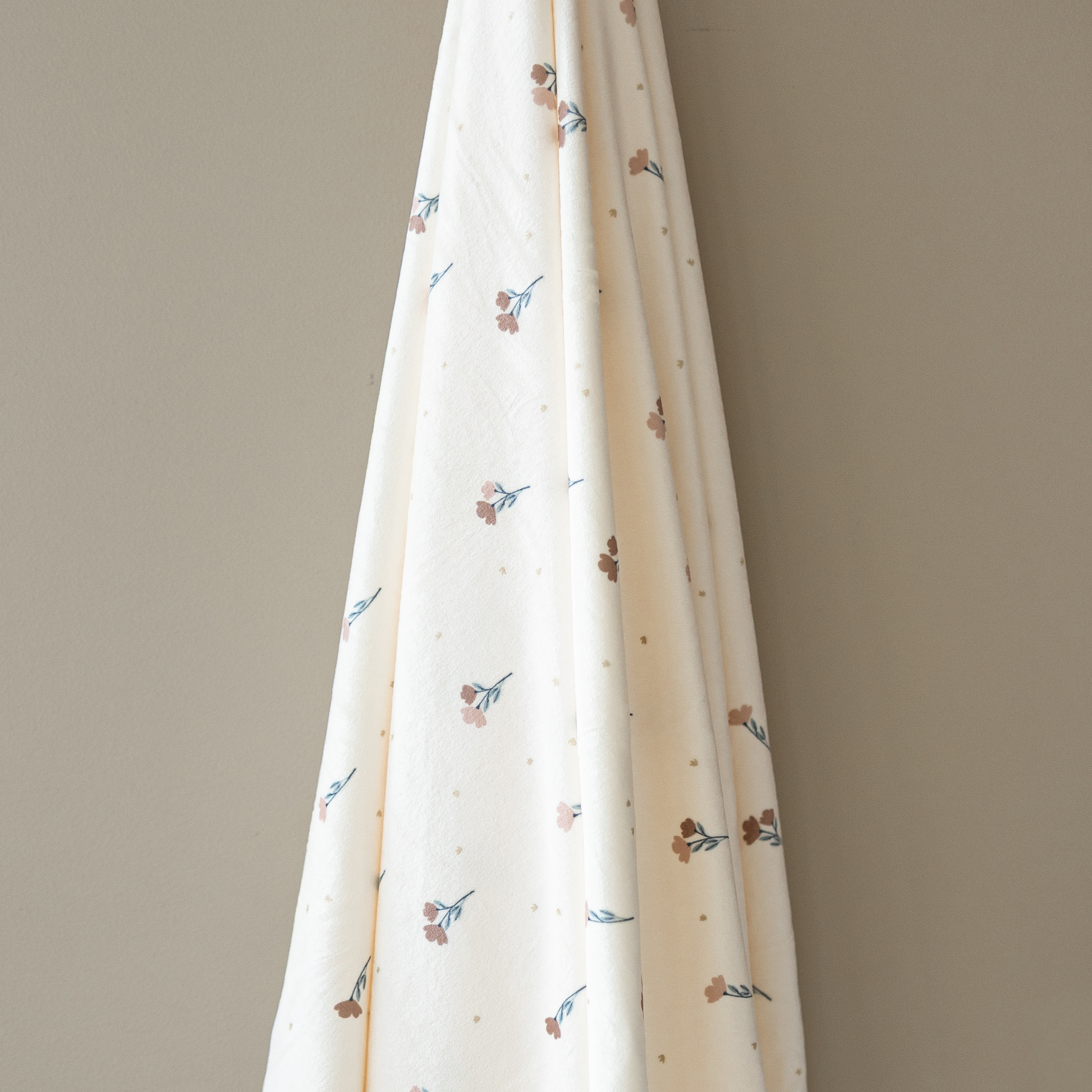 A floral minky stretch luxe swaddle that is hanging in front of a taupe wall. 