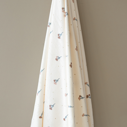 A floral minky stretch luxe swaddle that is hanging in front of a taupe wall. 