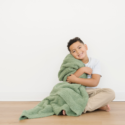 Boy snuggled with oversized Toddler Bamboni® blanket in Olive green color. 