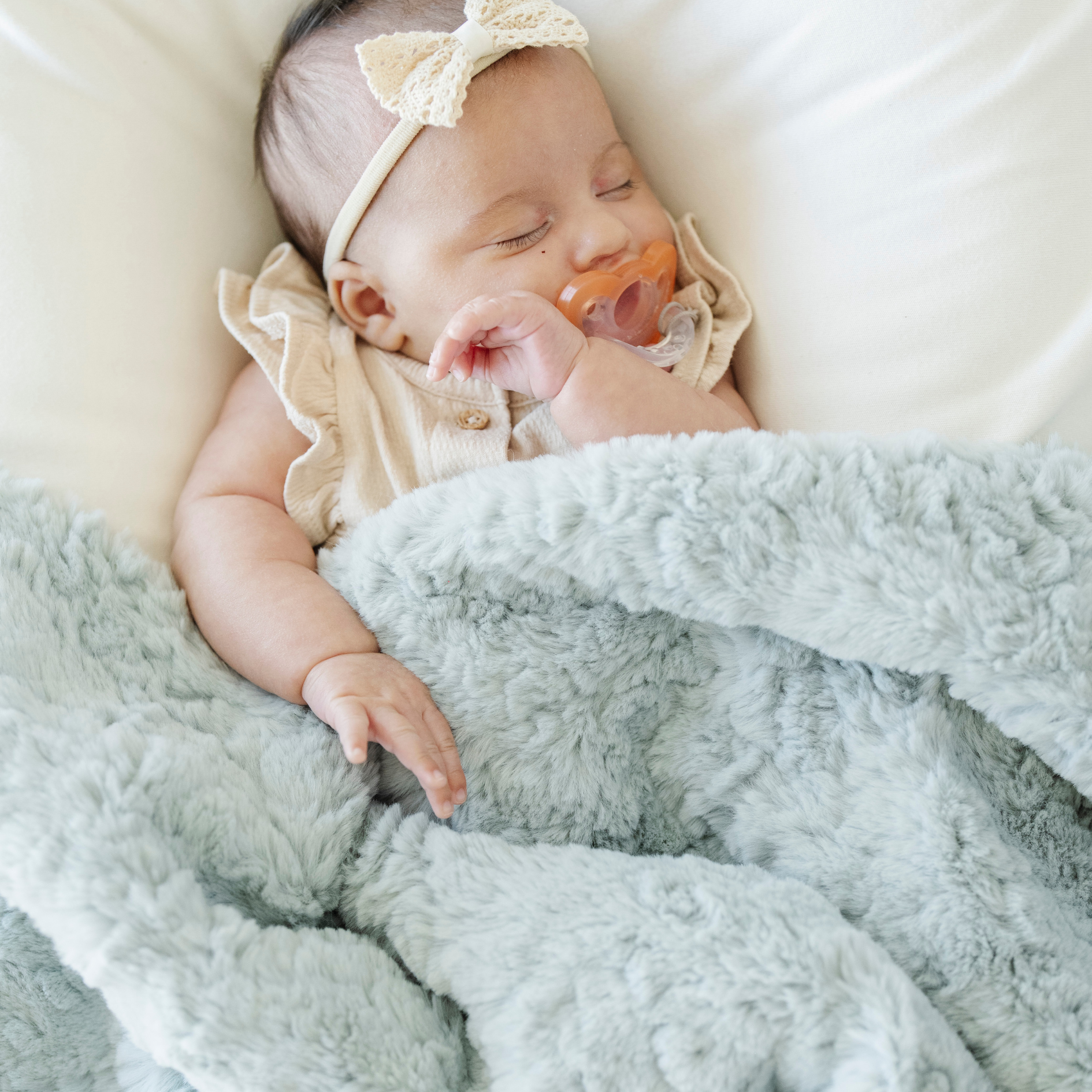 Baby girl sleeping with a mint green faux fur soft receiving baby blanket.