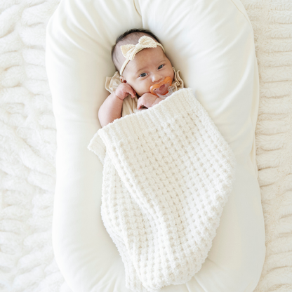 Newborn baby girl wrapped in a cream waffle knit mini blanket. 