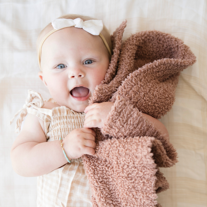 Baby girl holding Saranoni Mini Bamboni® baby blanket in French Rose color. 