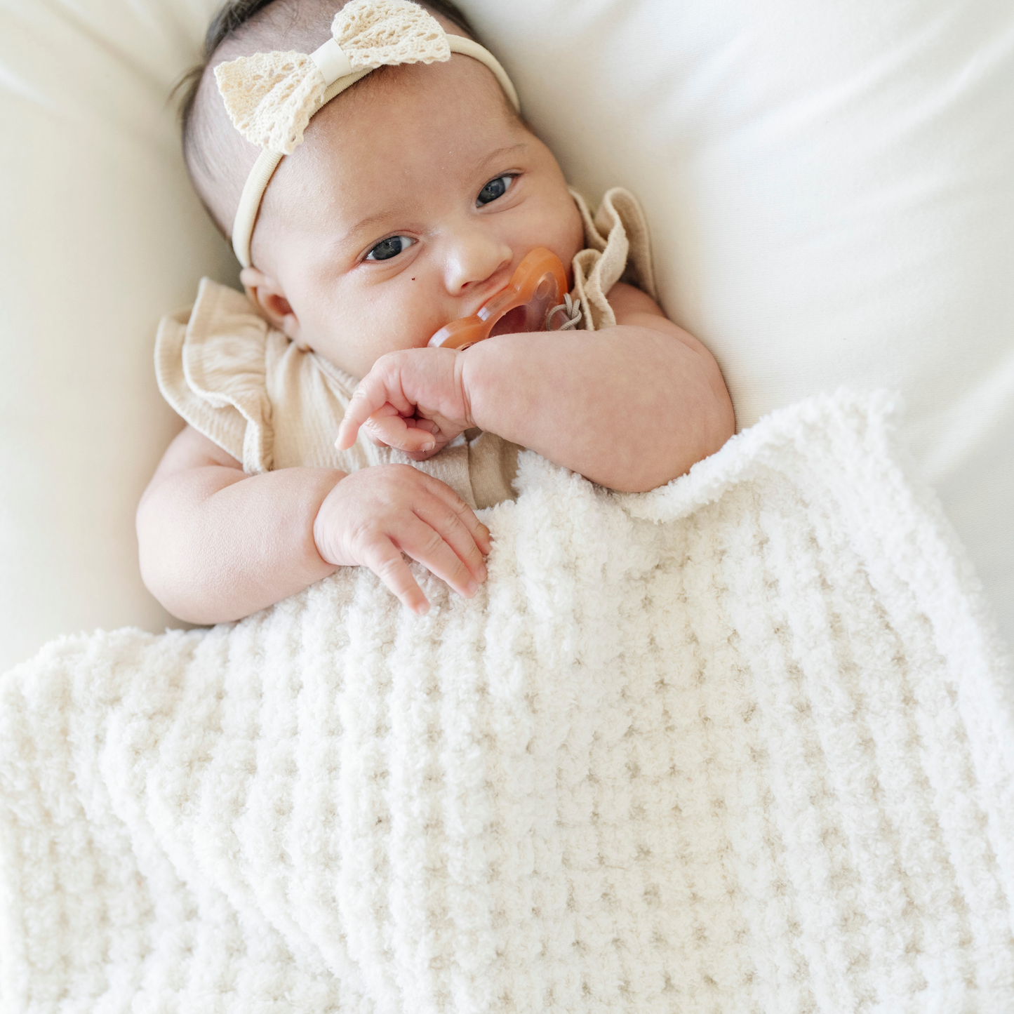 Baby girl snuggled with a cream waffle knit mini blanket. 