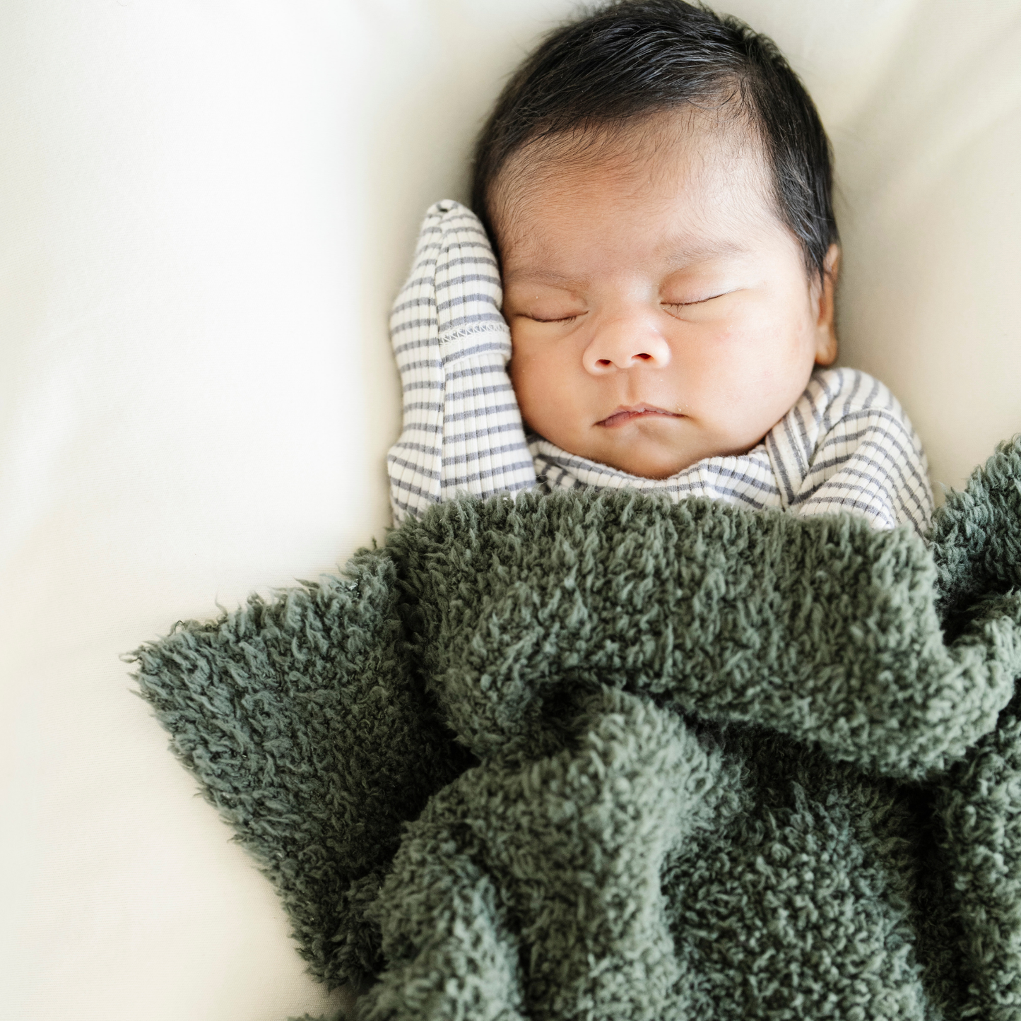Baby boy snuggled with Saranoni Bamboni® mini baby blanket in Juniper color. 