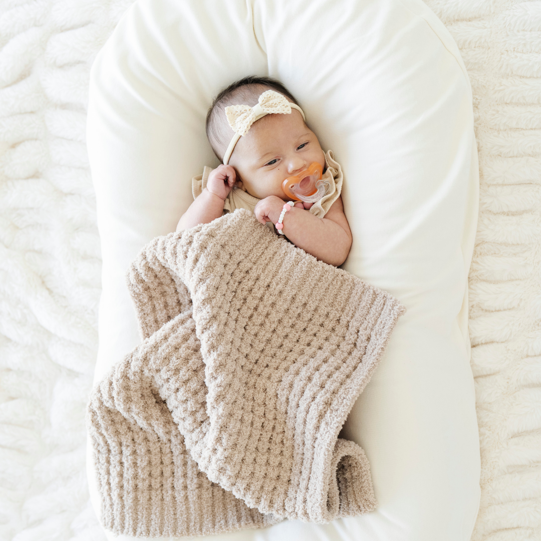 Baby girl snuggled with a wheat tan waffle knit mini blanket. 