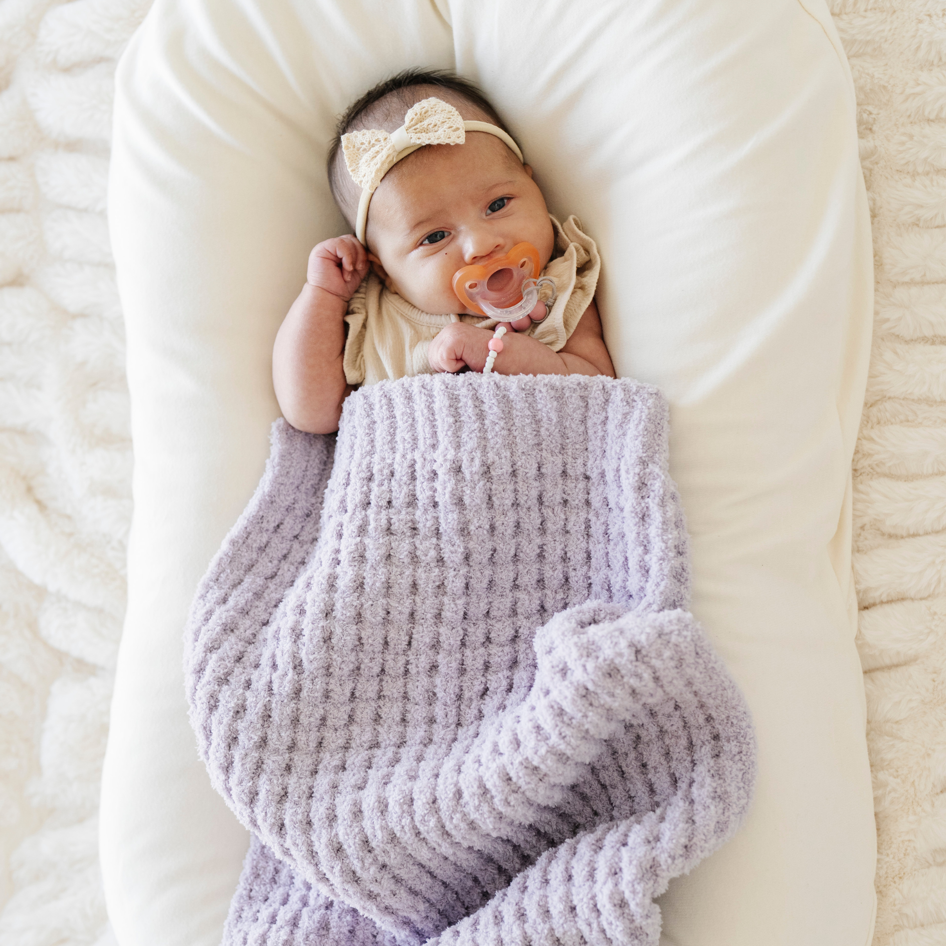 Baby girl snuggled with a purple waffle knit mini blanket. 