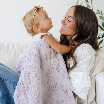 Mom holding baby girl snuggled with a purple soft receiving baby blanket. 
