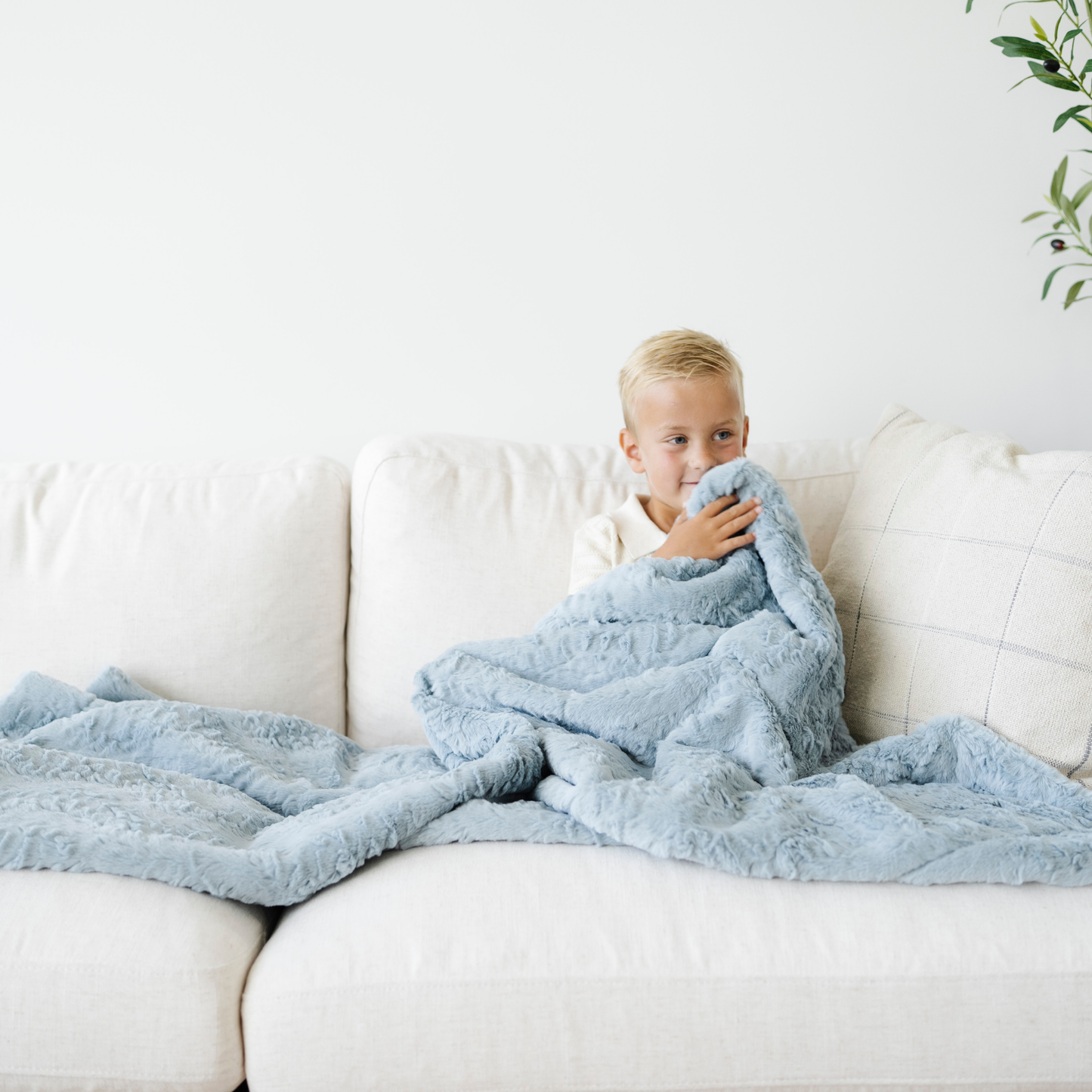 Boy snuggled on couch with a blue dream faux fur soft toddler blanket. 