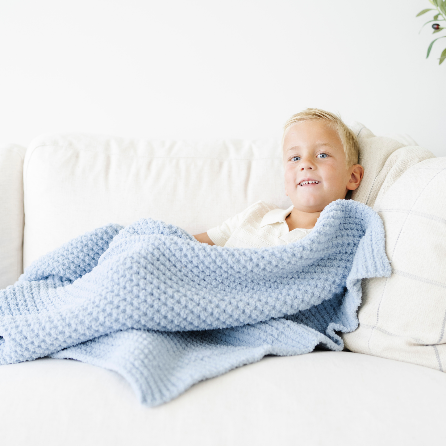 Boy snuggled on couch with a blue waffle knit toddler blanket. 