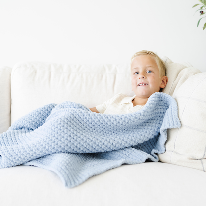 Boy snuggled on couch with a blue waffle knit toddler blanket. 