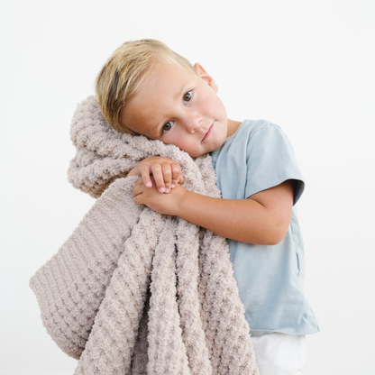 Little boy snuggled with a tan waffle knit soft toddler blanket. 
