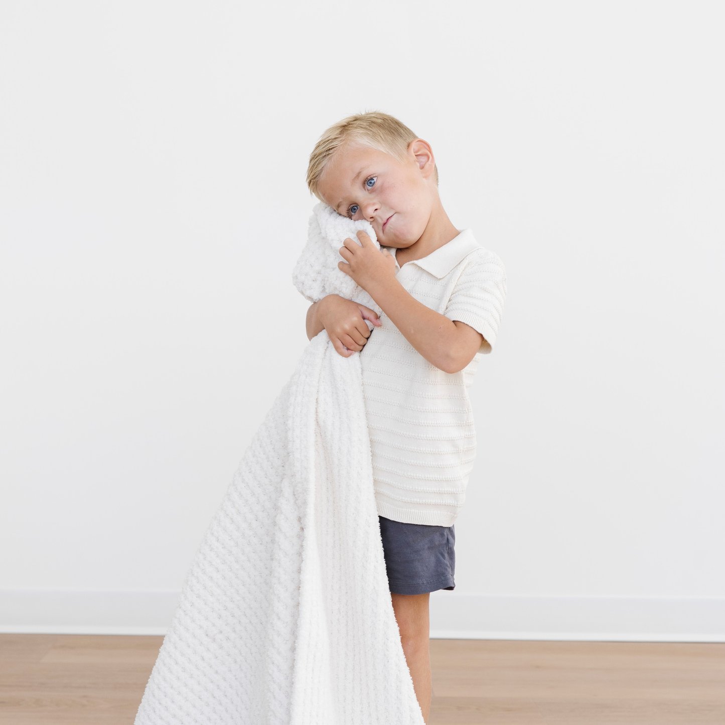 Boy snuggles a cream waffle knit cozy toddler blanket. 