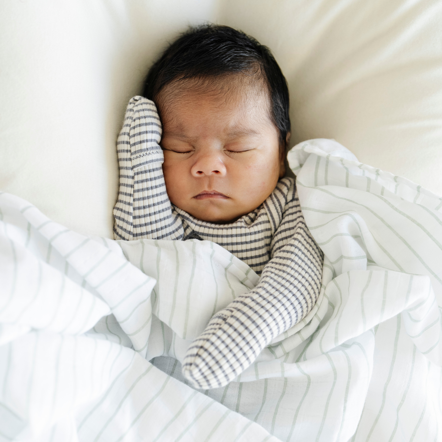 Baby boy snuggled with Saranoni Cotton Muslin Swaddle in Breezy Stripe. 