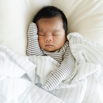Baby boy snuggled with Saranoni Cotton Muslin Swaddle in Breezy Stripe. 