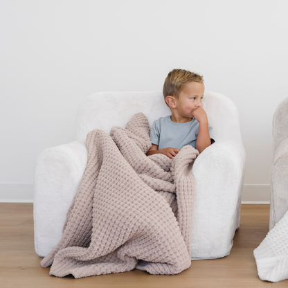 Little boy sits in a soft chair snuggling a tan waffle knit toddler blanket. 