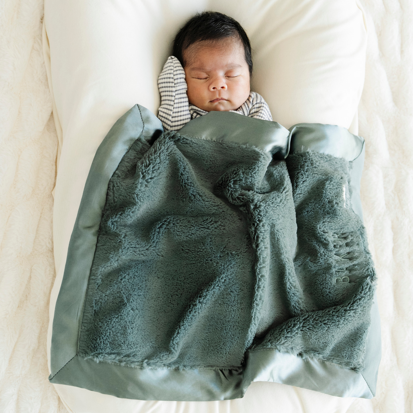 Baby boy snuggled in Evergreen Satin Border mini baby blanket. 